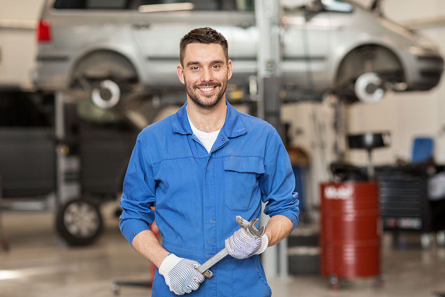 An ASE certified mechanic in a workshop in a blue uniform holding a wrench in Decatur, IL.