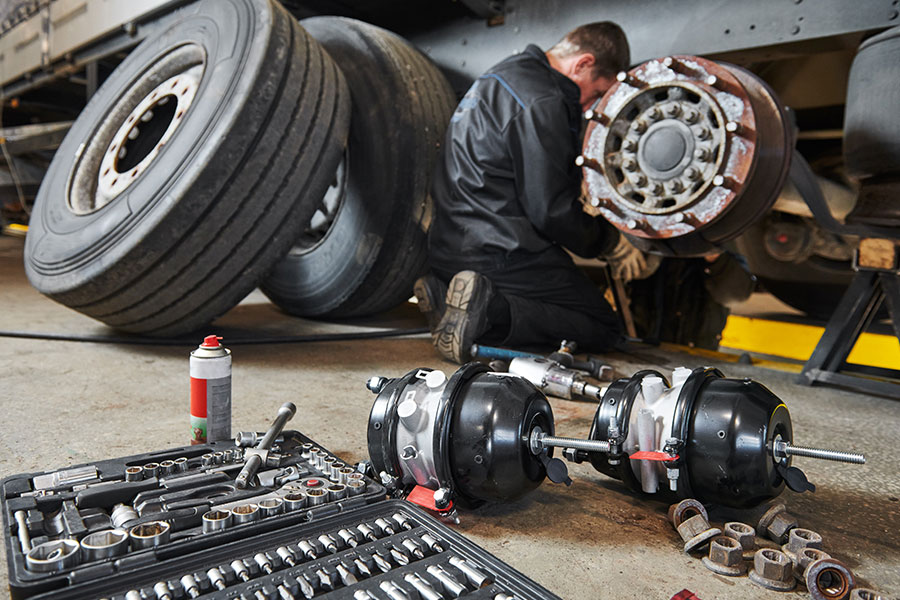 A mechanic in Decatur, IL replacing the braking system on a semi-truck and trailer. Tools scattered in a commercial repair shop.