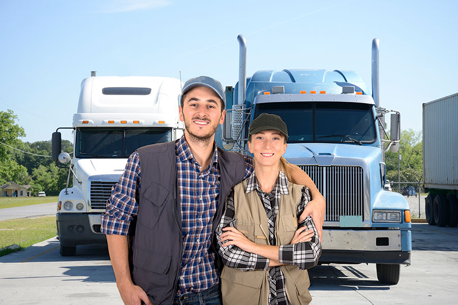 A male truck driver smiling and putting his arm around a female truck driver as they stand in front of their two semi-trucks in Decatur, IL.