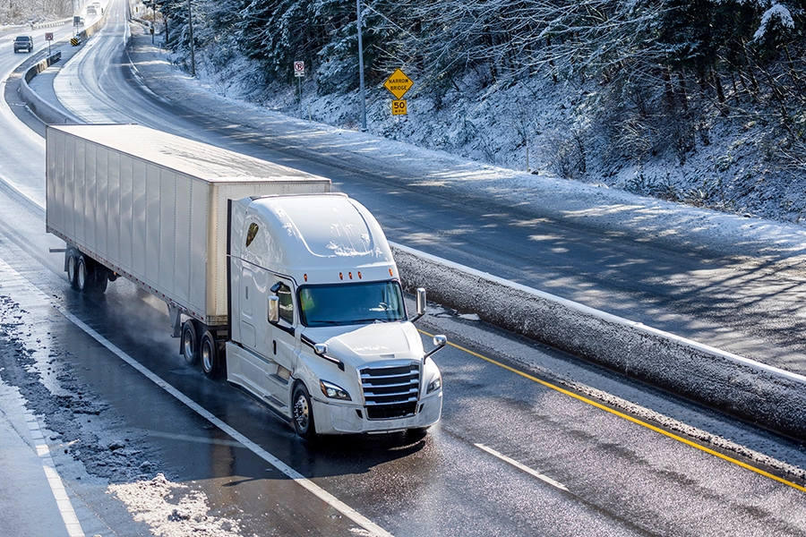 A white diesel truck on an interstate highway, driving through Decatur, IL, during the winter.