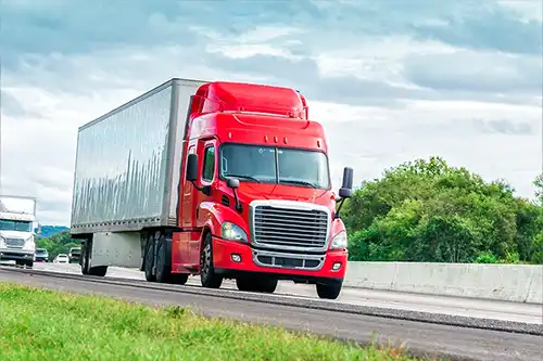 A red semi-truck driving in Decatur, IL, after having been inspected by Decatur Trailer Sales & Service.