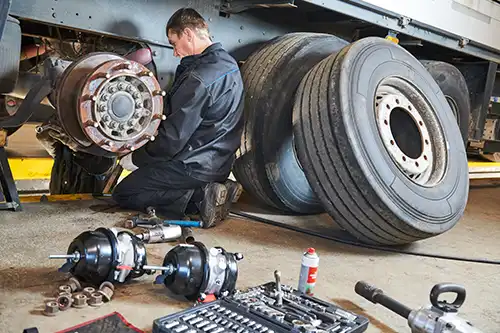 Decatur Trailer Sales & Service Inc. – Mechanic with tools sitting by him working on a brake repair on a semi-truck in Decatur, IL.