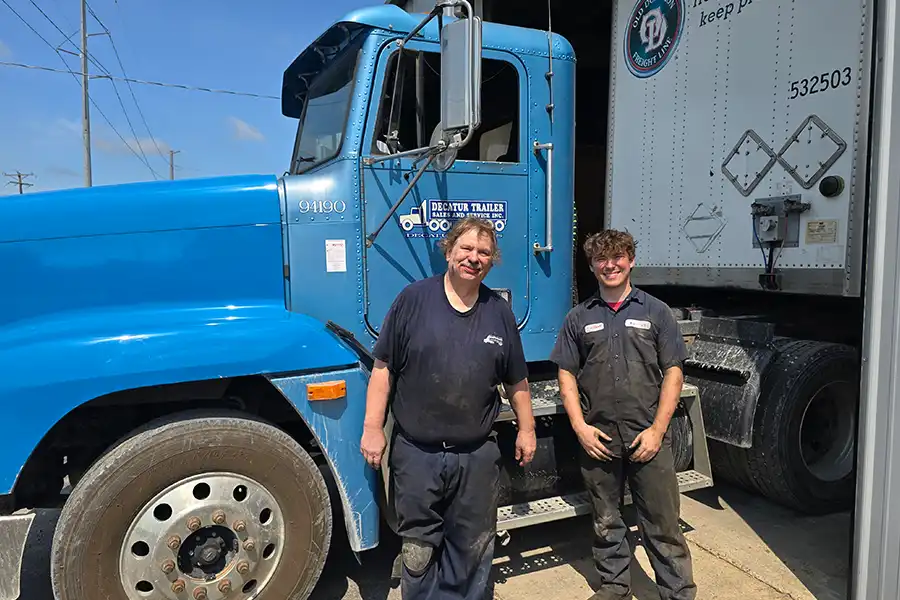 Two employees at Decatur Trailer Sales & Service smiling in front of a blue semi truck.