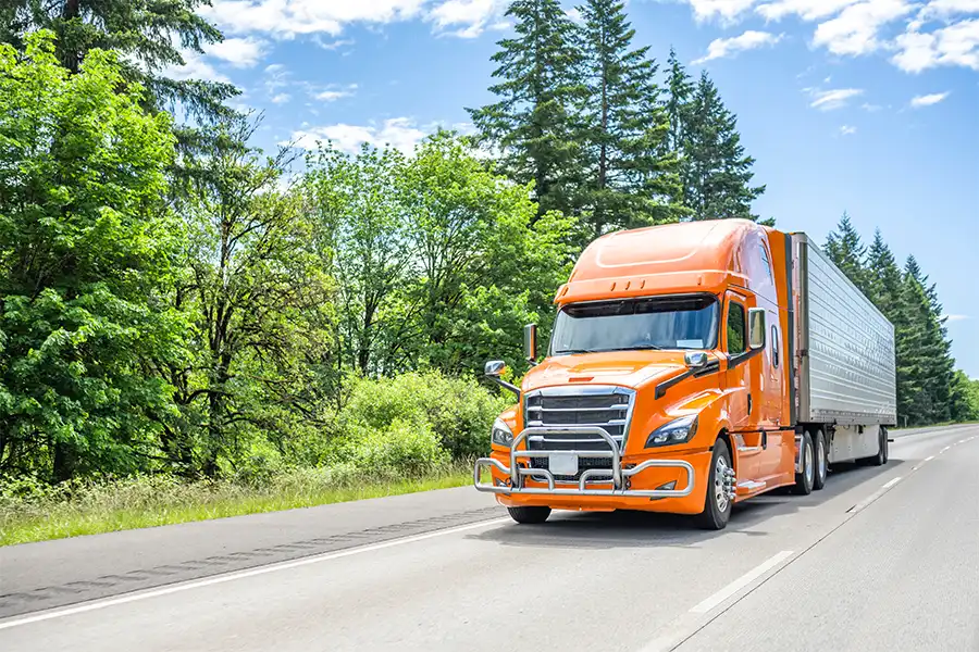 Decatur Trailer Sales & Service—An orange semi-truck driving through Decatur, IL during the summer season.