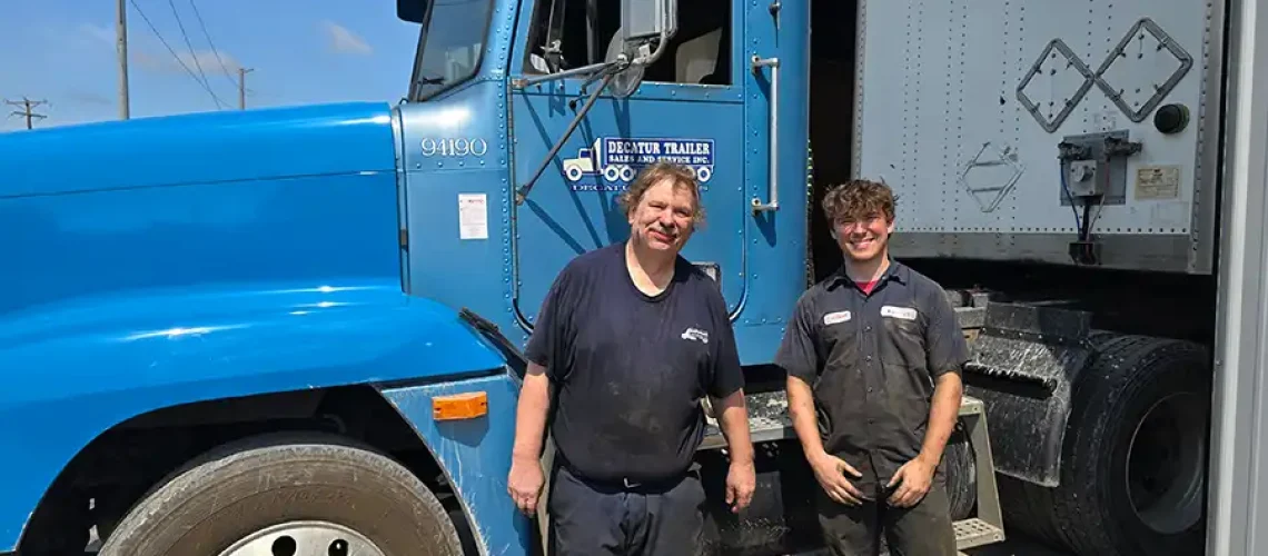 Two employees at Decatur Trailer Sales & Service smiling in front of a blue semi truck.