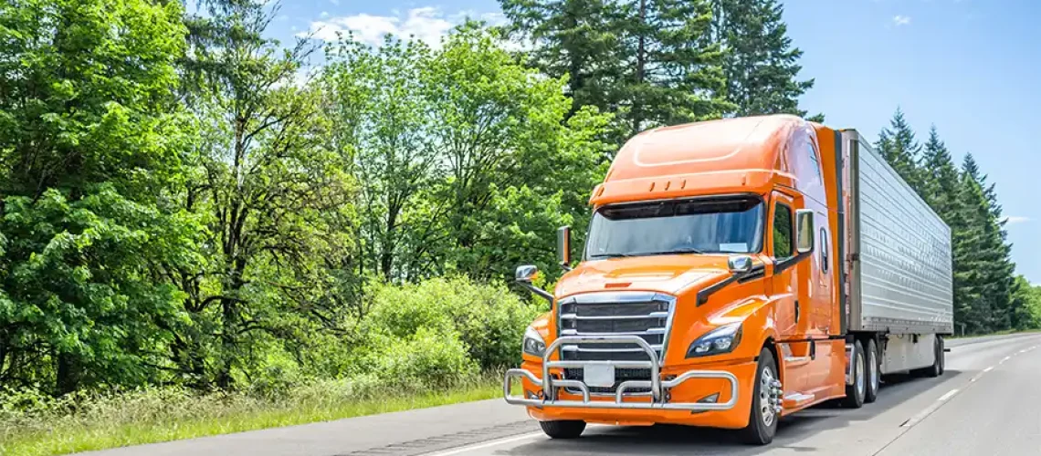 Decatur Trailer Sales & Service—An orange semi-truck driving through Decatur, IL during the summer season.