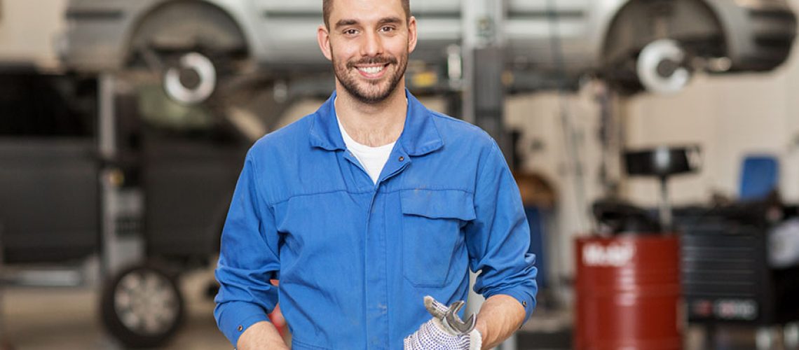 An ASE certified mechanic in a workshop in a blue uniform holding a wrench in Decatur, IL.