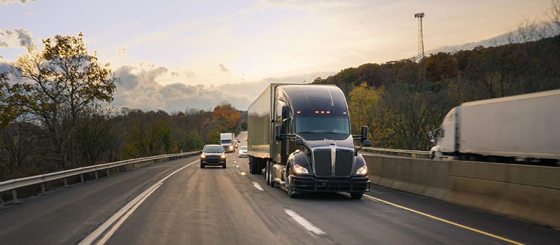 A black semi-truck driving on a highway for a long-distance trip that requires safety tips for winter weather in Decatur, IL.