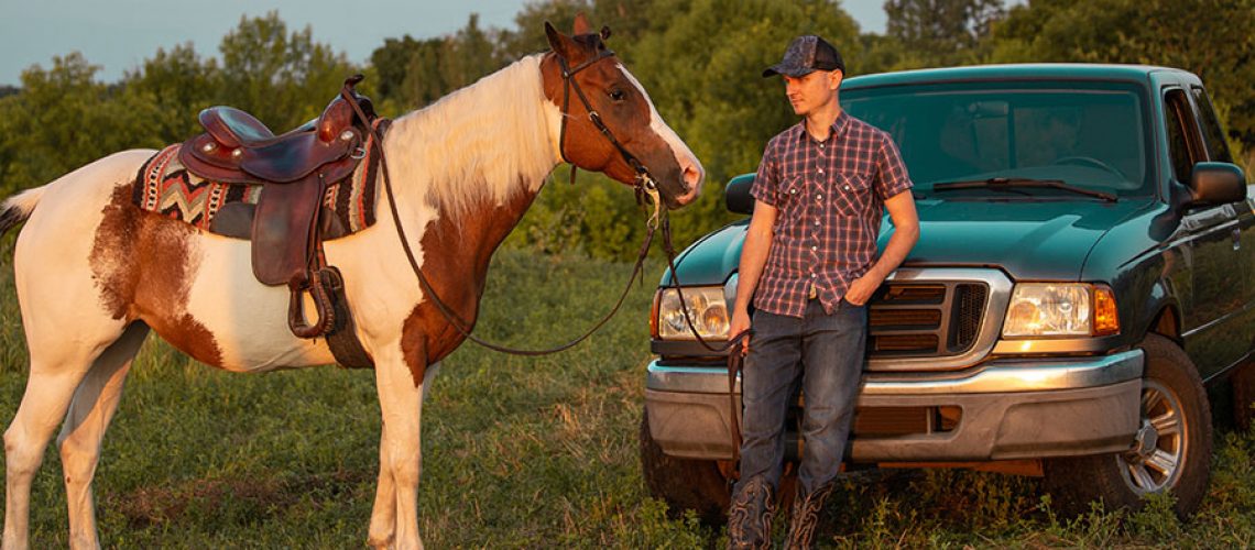 A man in a flannel shirt on a ranch holding the reins of a horse and leaning against his pickup truck in Decatur, IL.
