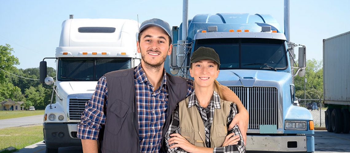A male truck driver smiling and putting his arm around a female truck driver as they stand in front of their two semi-trucks in Decatur, IL.